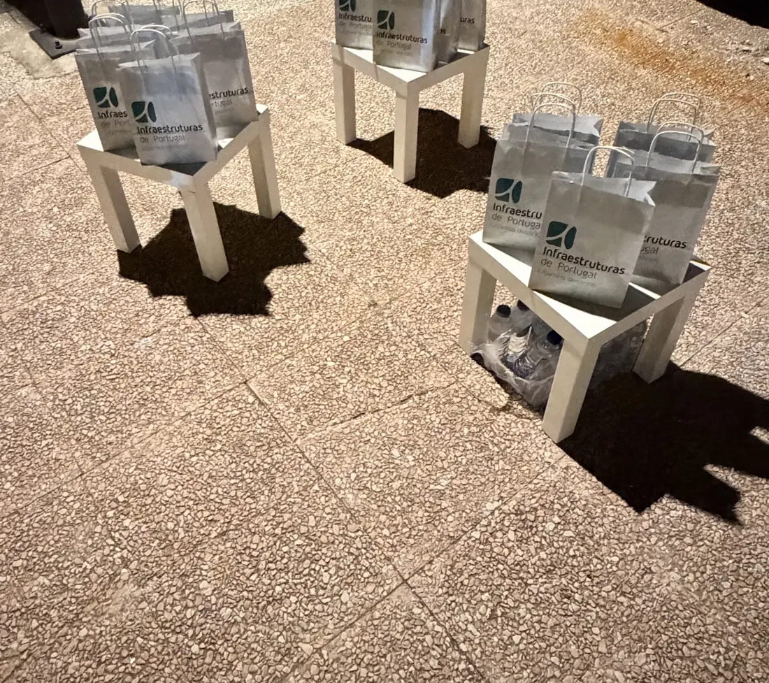 Sacos da Infraestruturas de Portugal prontos a distribuir em mesas brancas, à noite
